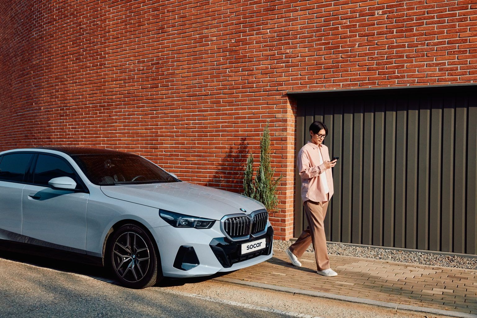 빨간색 벽돌 건물 앞에서 BMW 차량 앞을 지나가는 남성 이미지